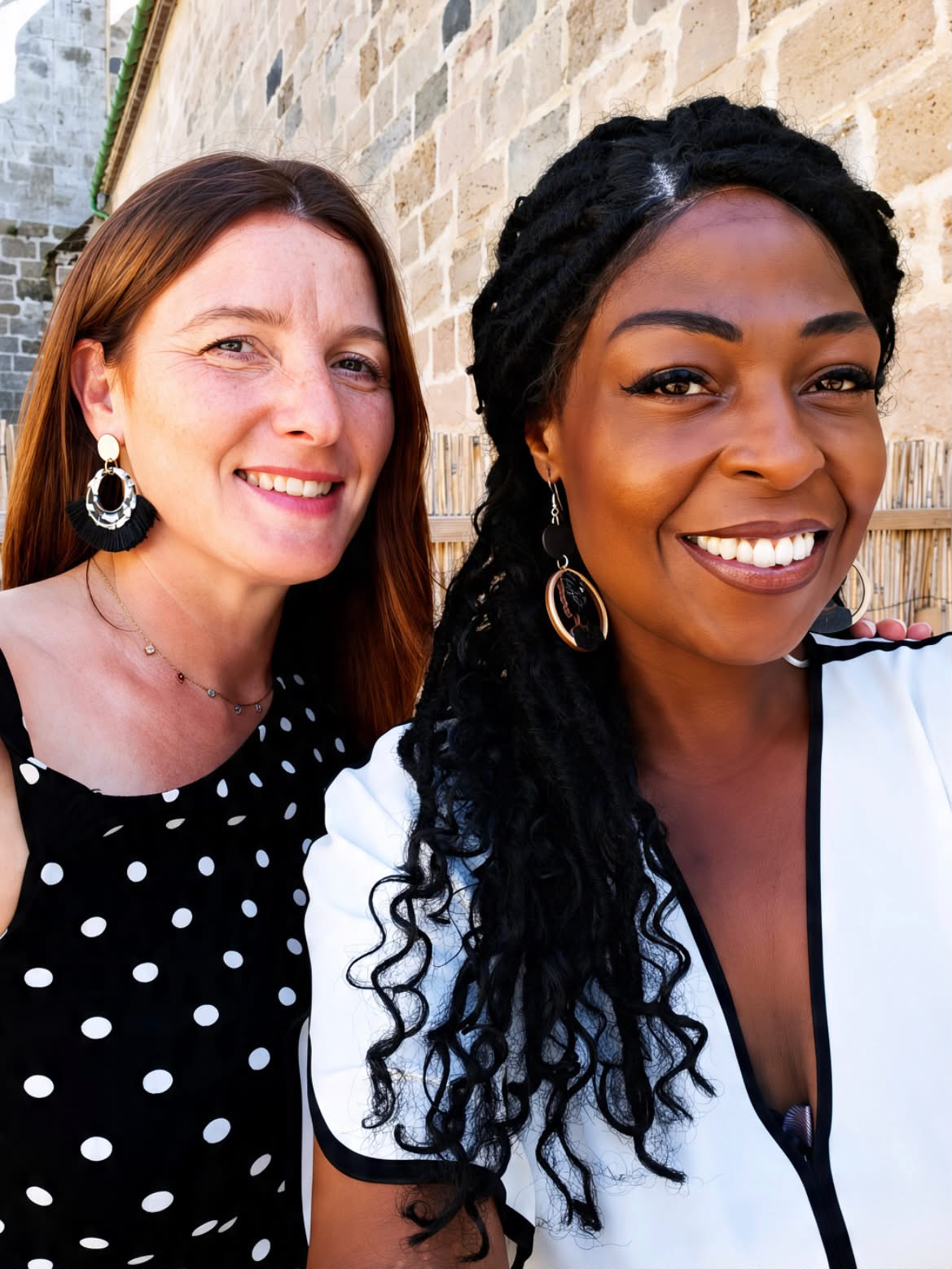 Les deux chanteuses d’Échos d’âmes, souriantes, devant un mur de pierre
